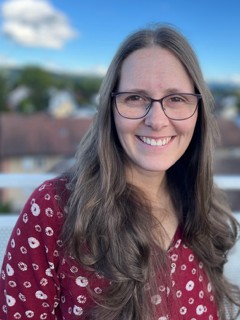 Freundlich lächelnde junge Frau mit braunen Augen, Brille und langen braunen Haaren.