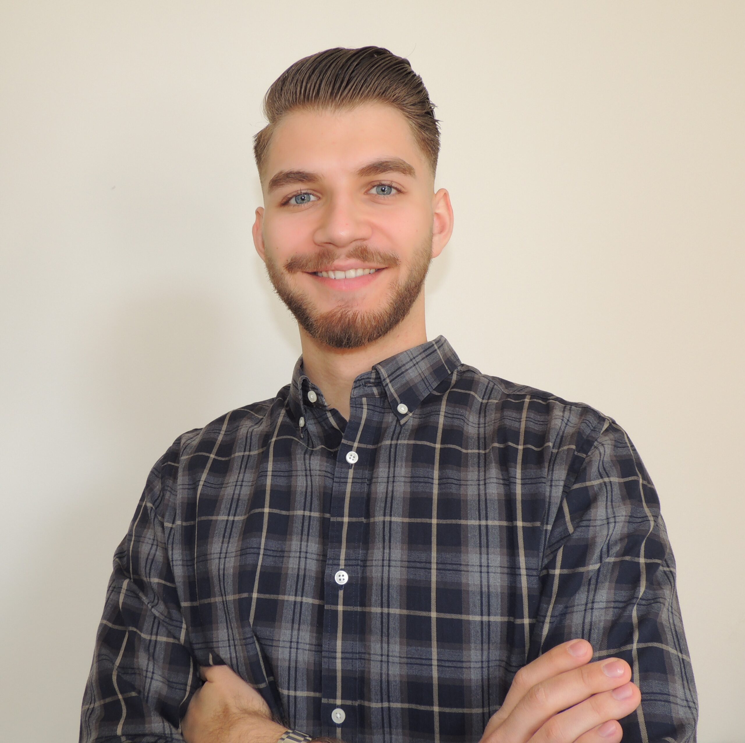 Freundlich lächelnder junger Mann mit blauen Augen, einem Vollbart und kurzen braunen Haaren.